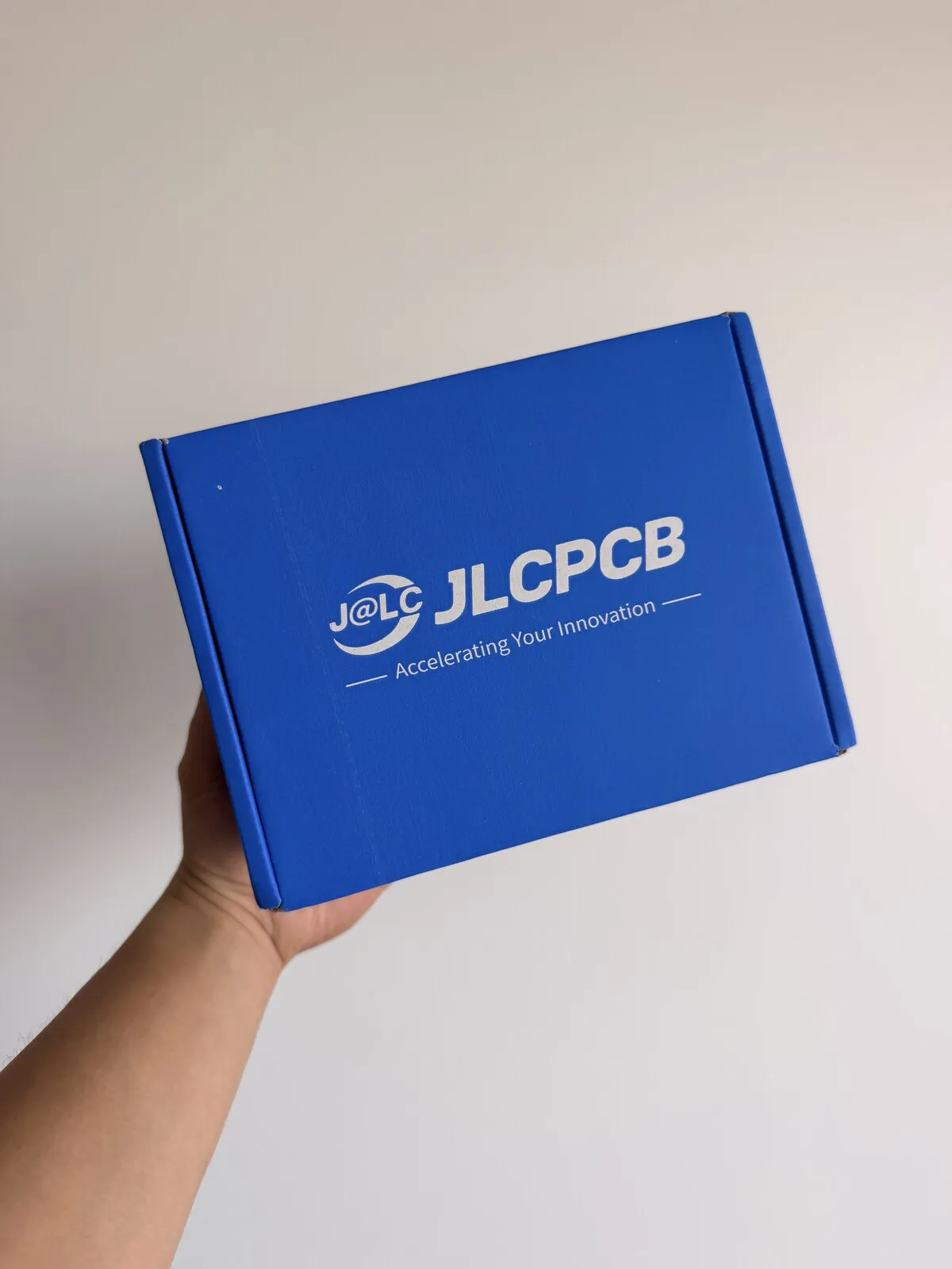 A hand holding the blue JLCPCB shipping box that contained the assembled circuit-board business cards.