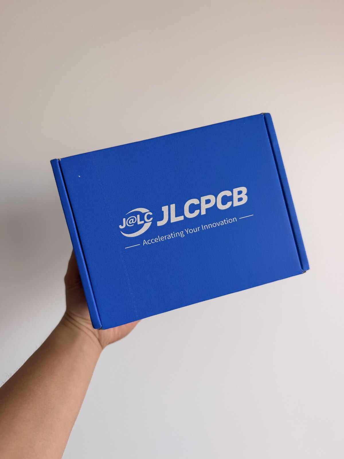 A hand holding the blue JLCPCB shipping box that contained the assembled circuit-board business cards.