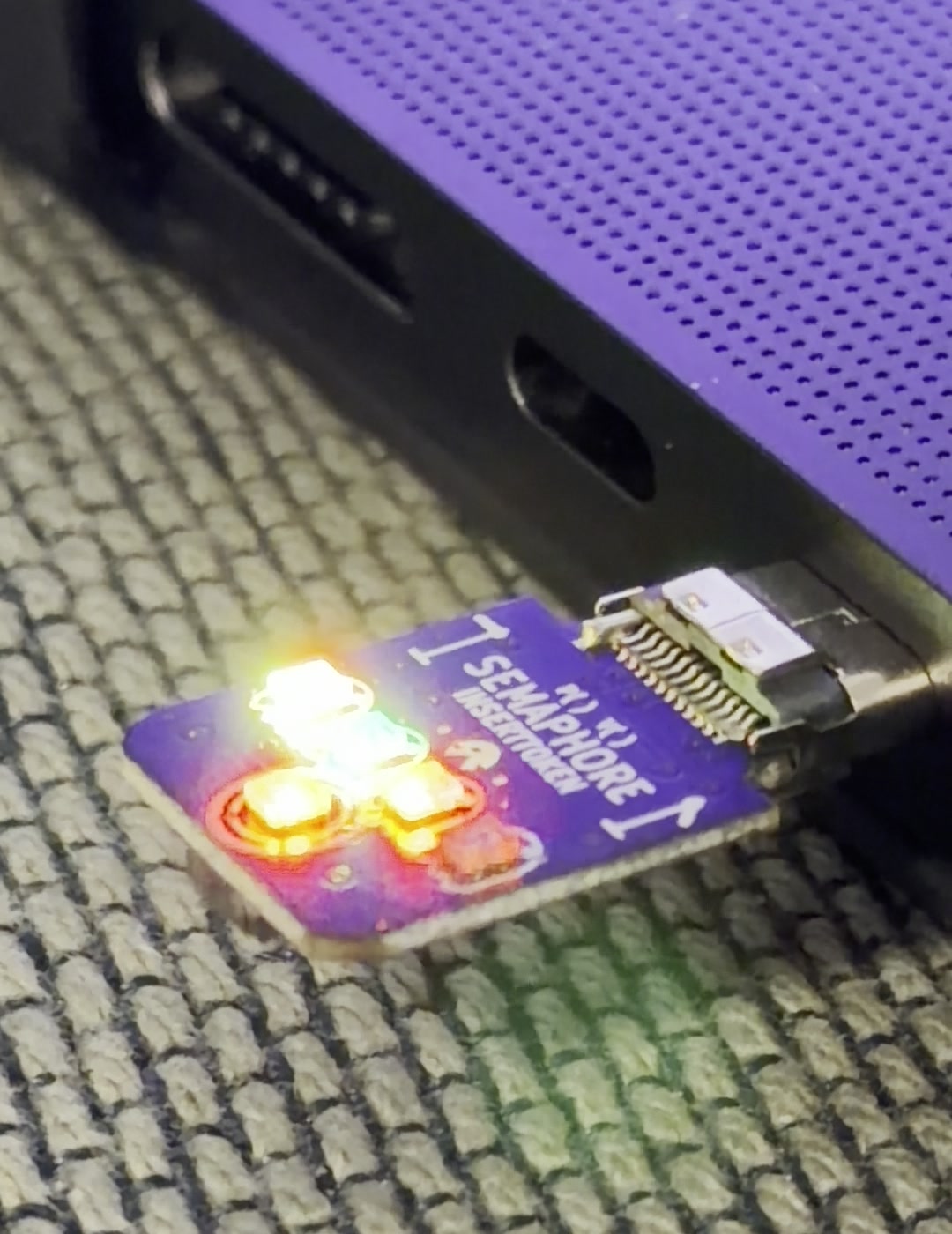The first Semaphore rev-F board plugged into a MacBook USB-C port, its LEDs glowing warm amber