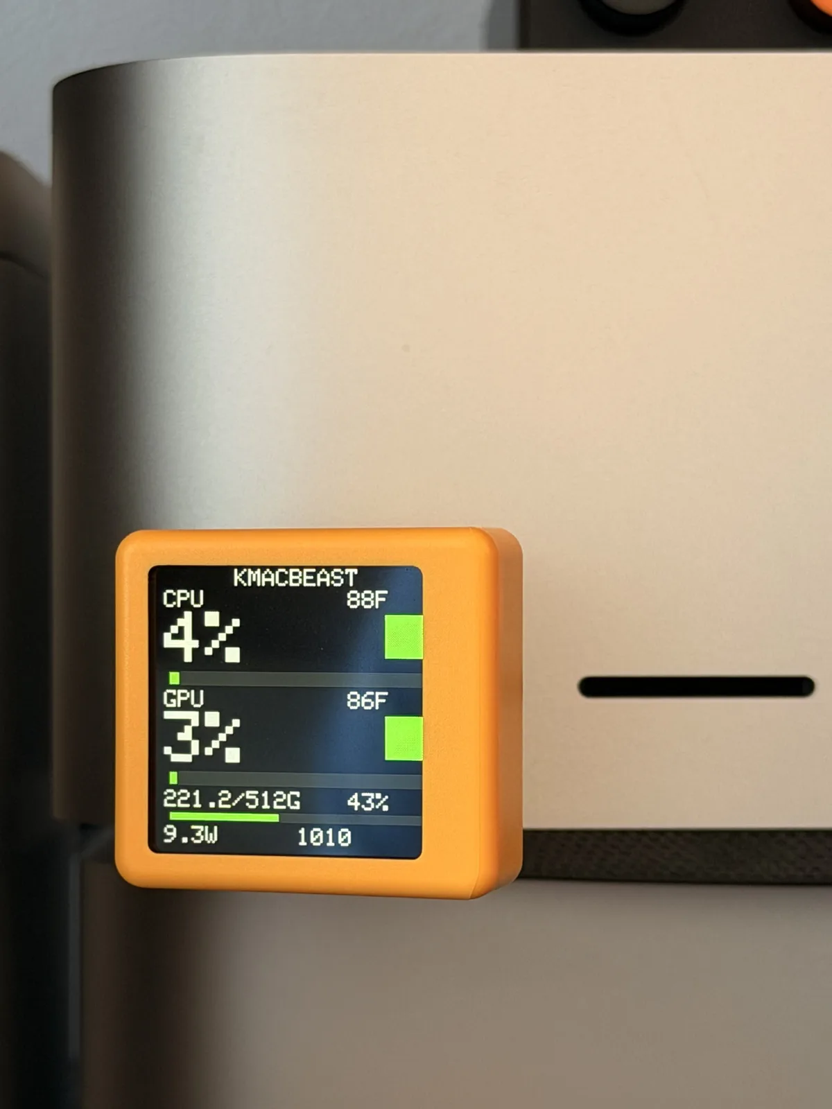 A SmallTV cube plugged directly into the front USB-C port of a Mac Studio, next to the SD slot, showing the KMACBEAST dashboard